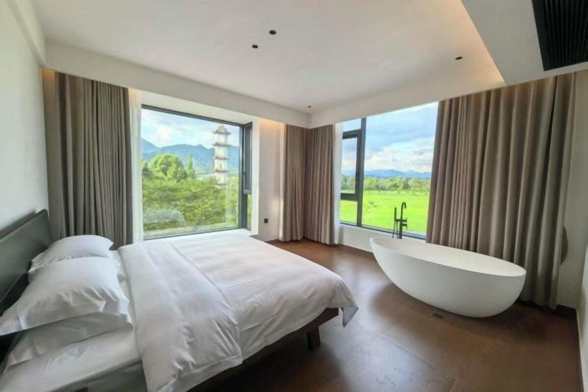 Ein modernes Schlafzimmer mit einem großen Bett, einer freistehenden Badewanne und Blick auf eine Pagode durch große Fenster.