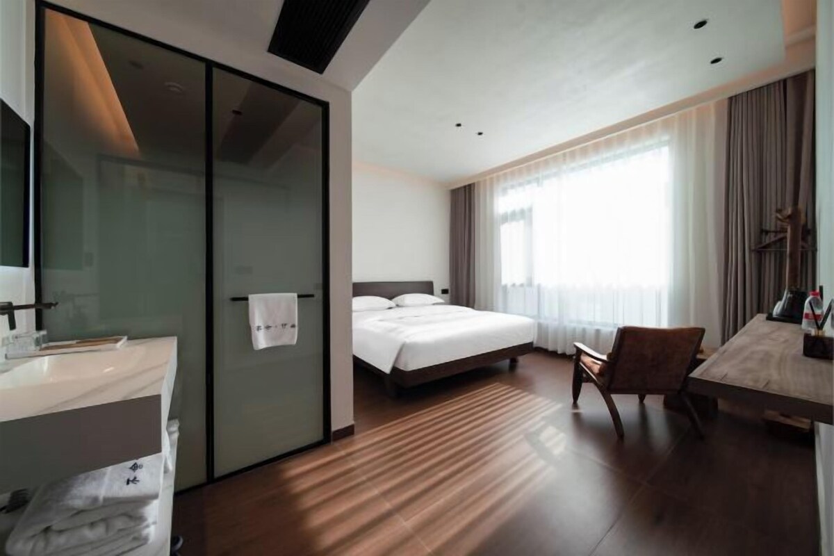A hotel room with a bed, a desk, a chair, a bathroom with a mirror, and a window with curtains.