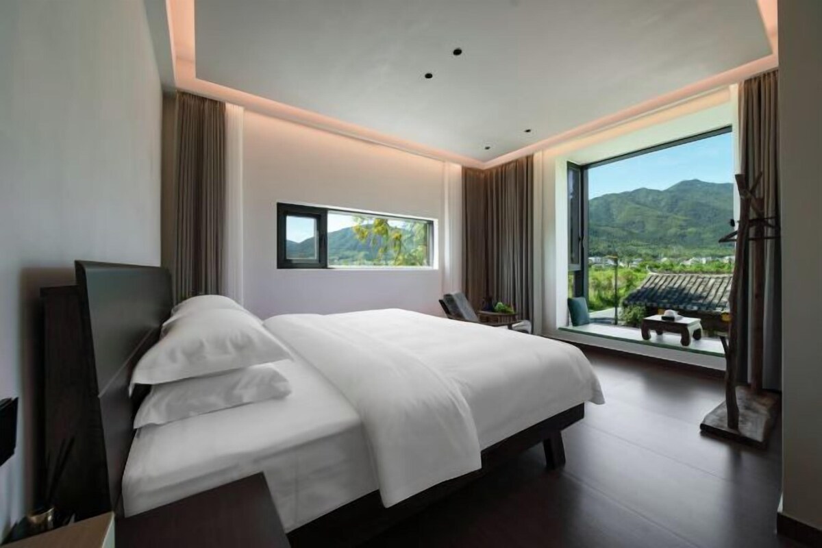 Ein modernes Hotelzimmer mit einem großen Bett, einem Fernseher und einem Fenster mit Bergblick.