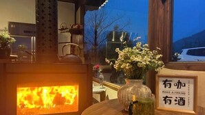 Ett mysigt rum med en vedeldad kamin, ett bord med en vas med blommor och en skylt med text på ett främmande språk.