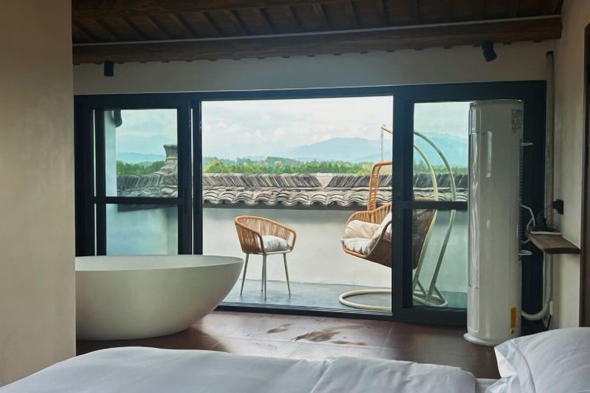 A room with a large bathtub, a chair, and a view of a traditional roof through a glass door.