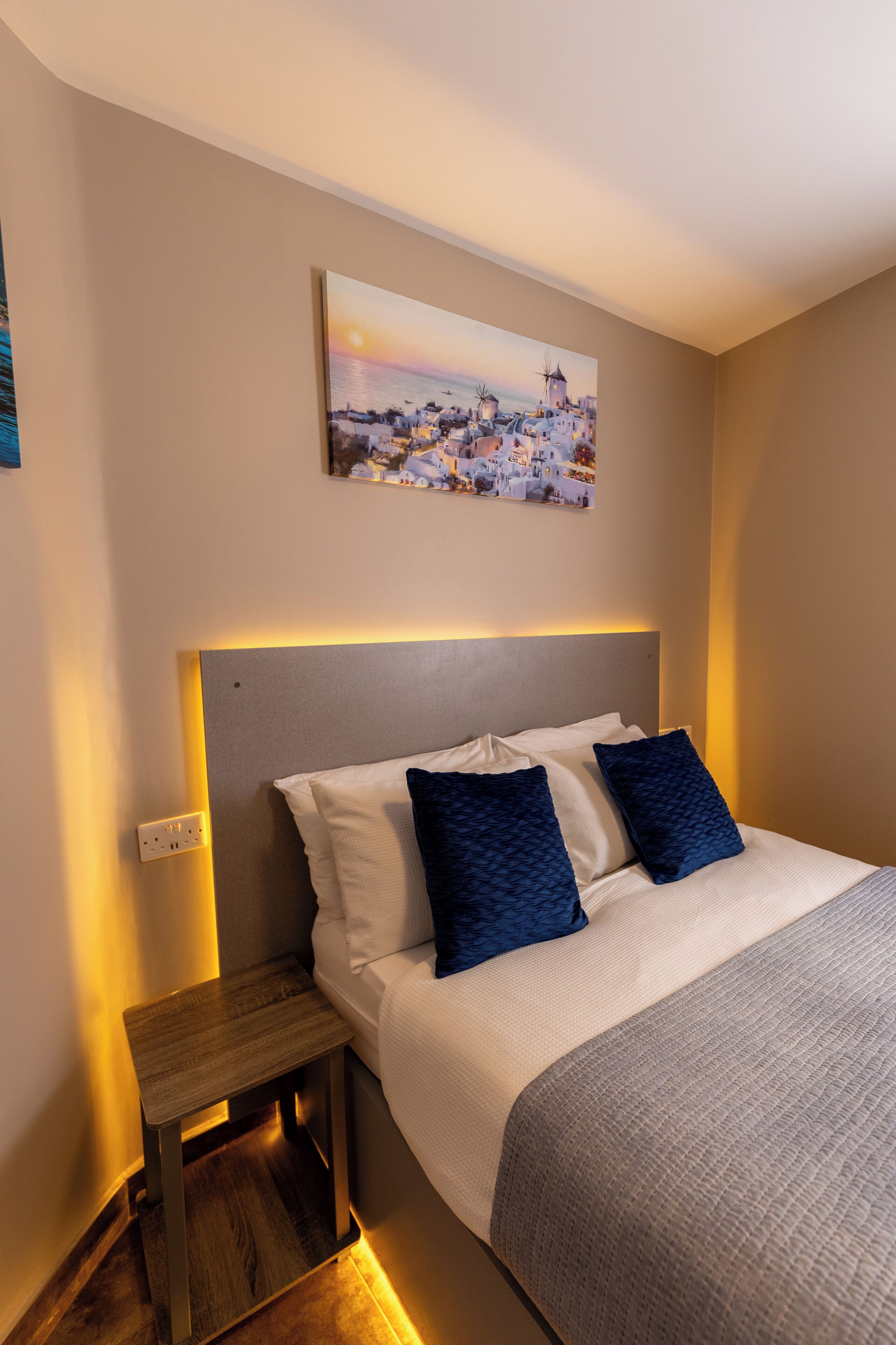 A neatly arranged bedroom with a bed, bedside table, and a wall-mounted painting.