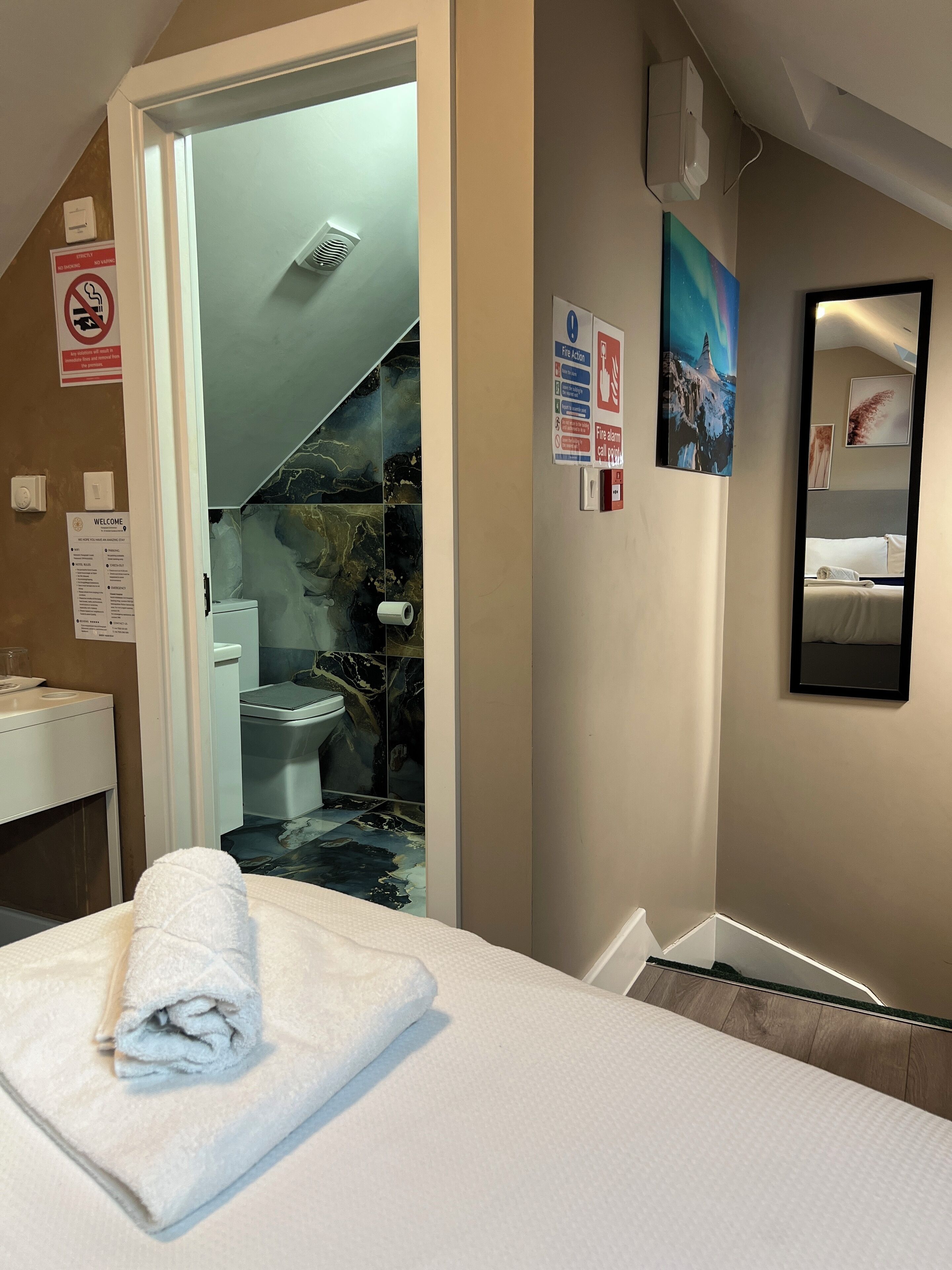 A hotel room with a bed, a bathroom with a toilet and sink, a towel on the bed, and a painting on the wall.