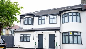 A two-story house with a dark-colored front door, a small porch with two potted plants, and a driveway. -  Rest Inn Edmonton (London)