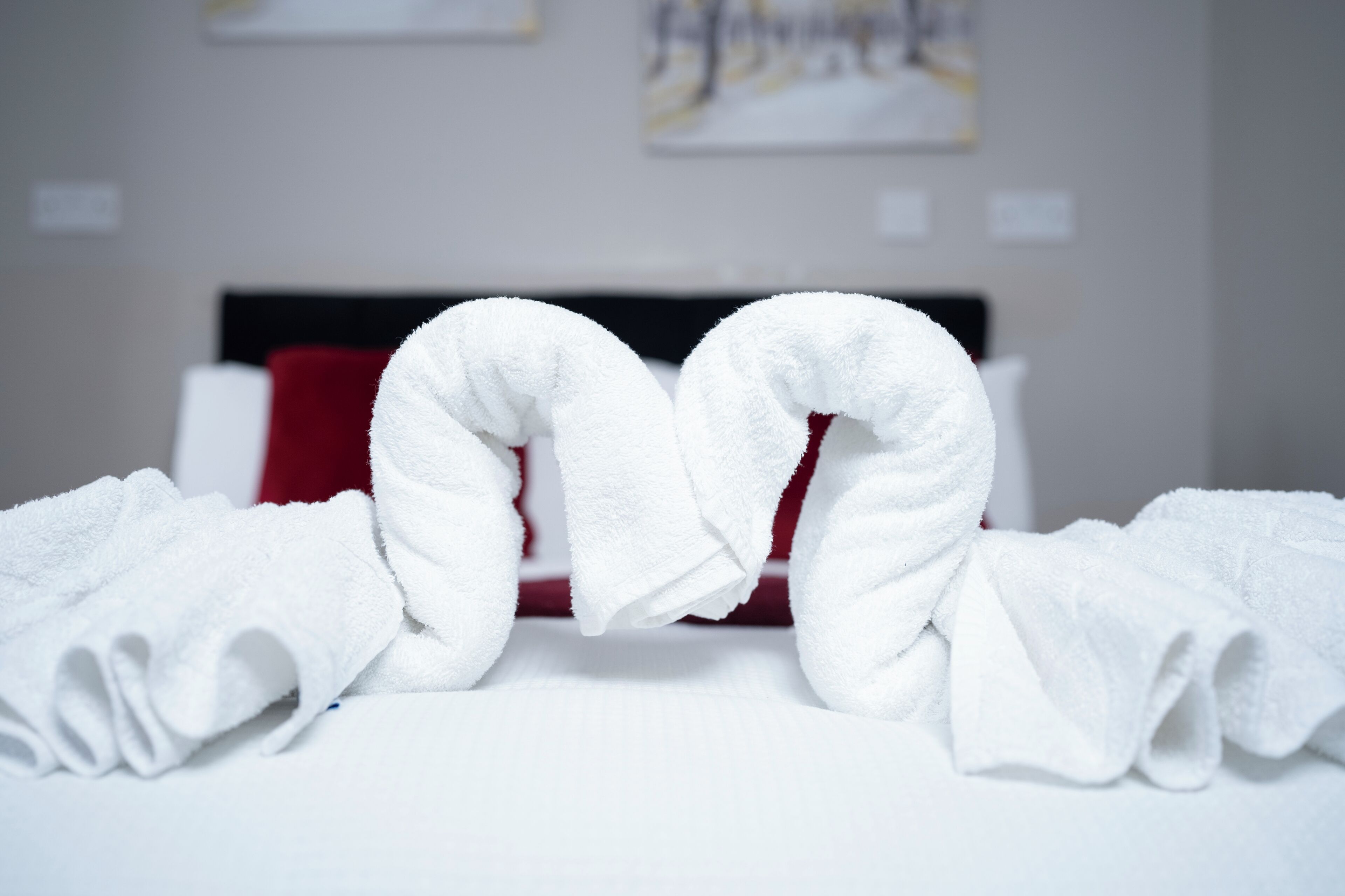 Neatly folded white towels arranged in a heart shape on a bed with a red headboard.