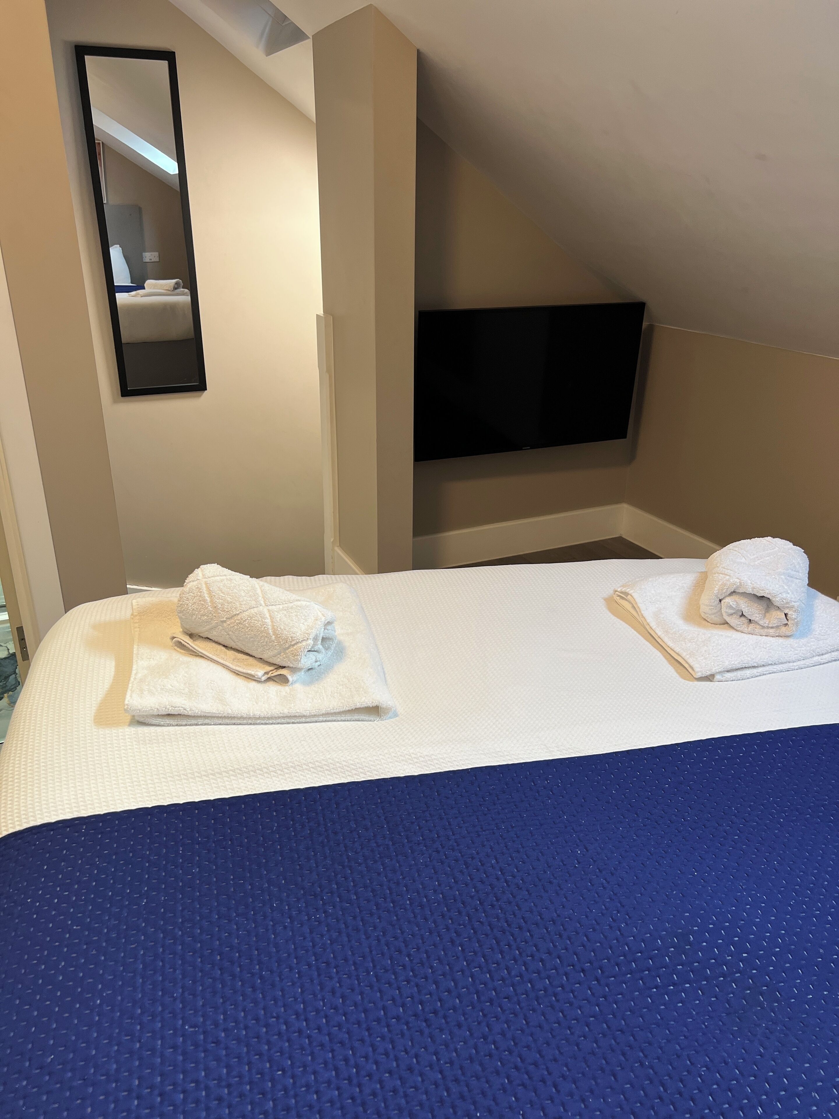A hotel room with a bed, two towels, a flat-screen TV, and a mirror.