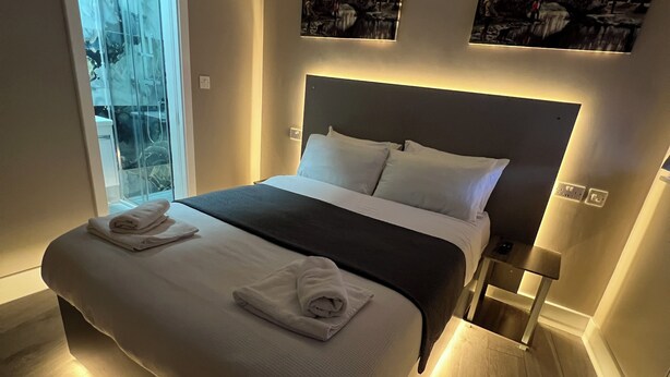 A modern bedroom with a large bed, a glass door leading to a balcony, and two wall-mounted artworks. -  Rest Inn Edmonton (London)
