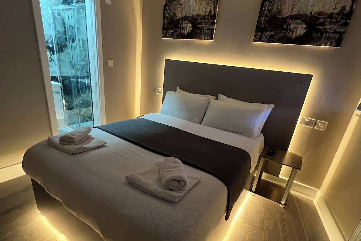 A modern bedroom with a large bed, a glass door leading to a balcony, and two wall-mounted artworks.