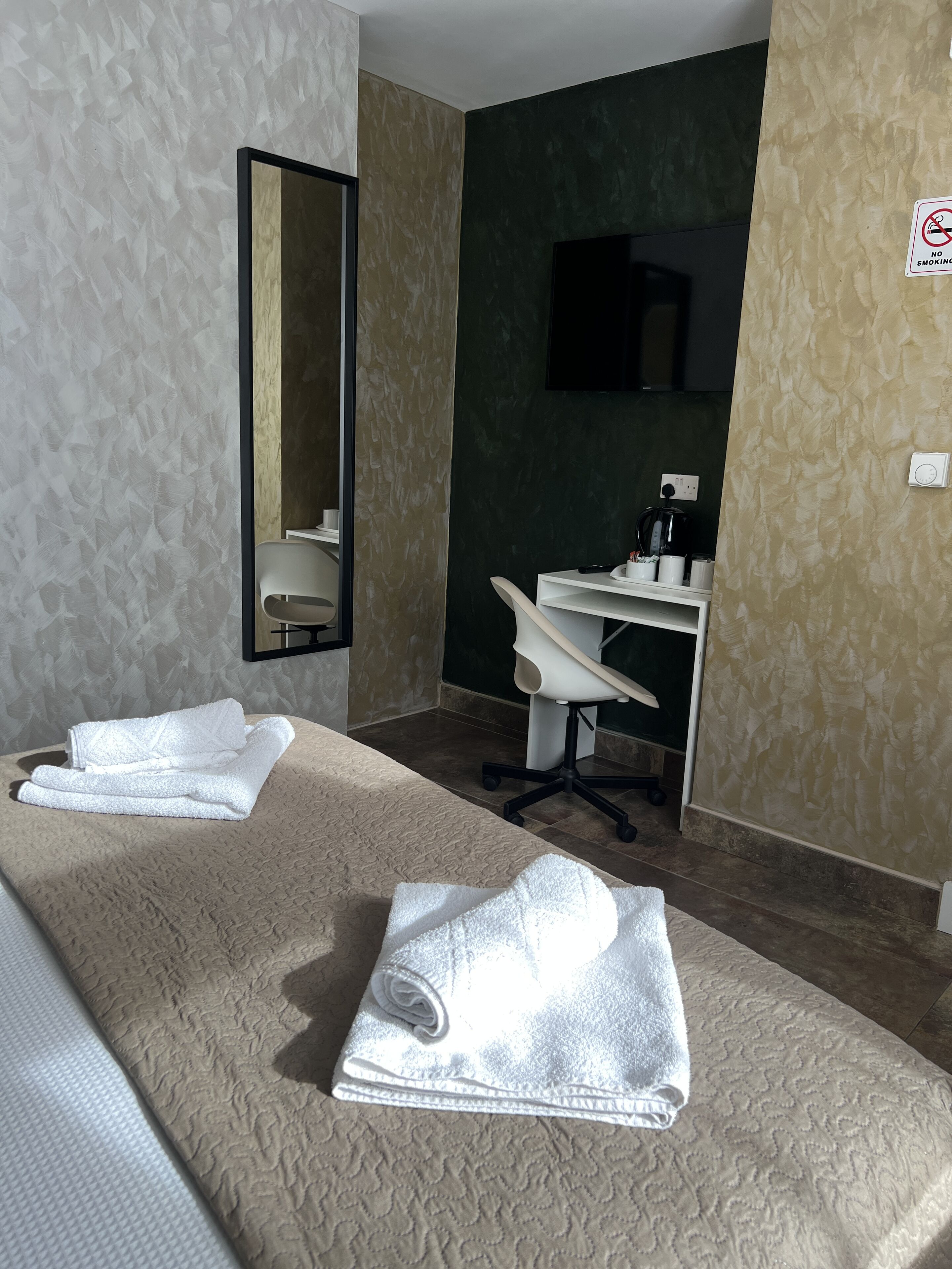 A hotel room with a bed, two towels, a desk, a chair, a mirror, and a TV.