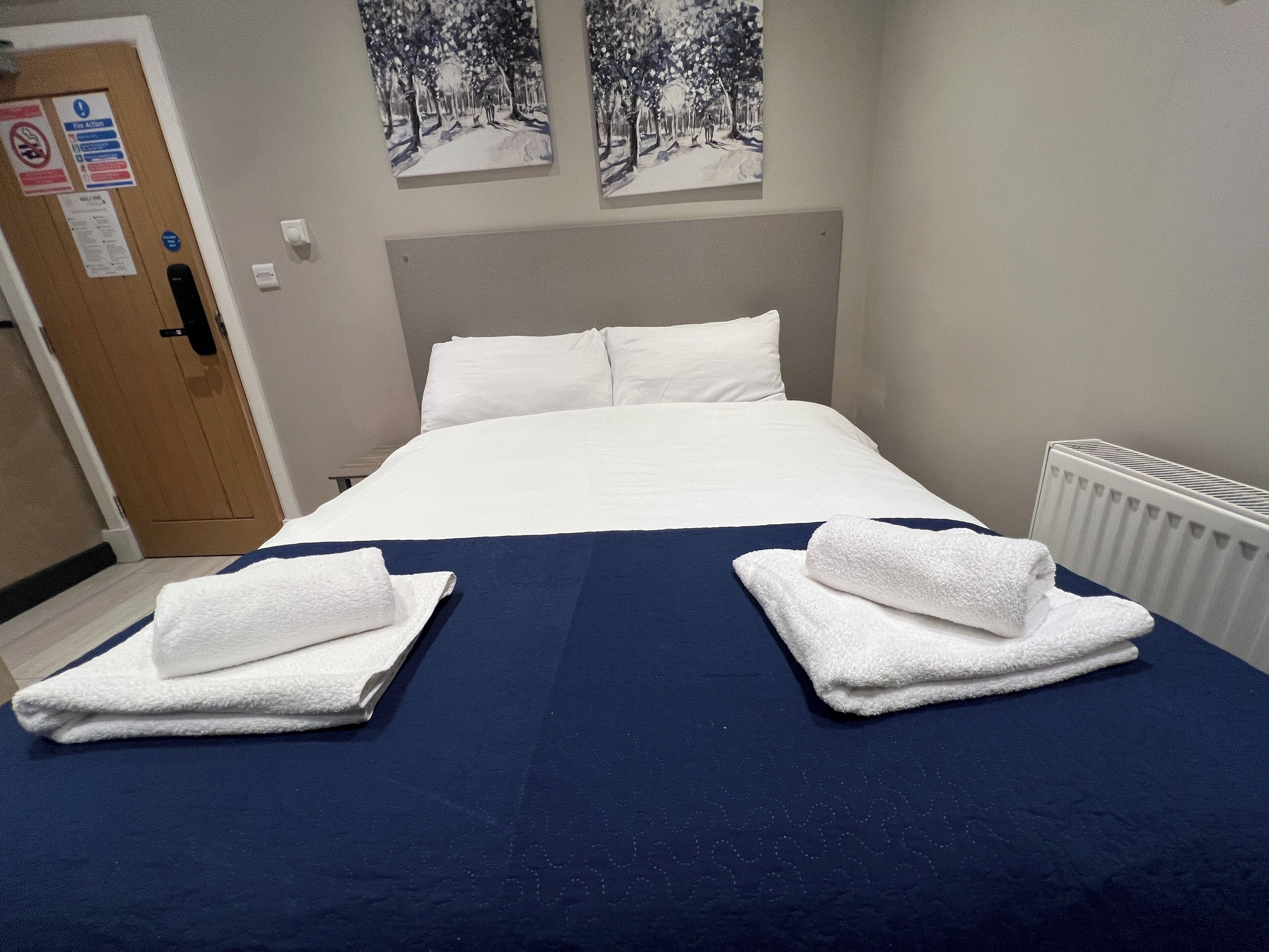 Un letto ben rifatto con lenzuola bianche e una coperta blu, due asciugamani bianchi sul letto e due quadri appesi alla parete sopra il letto.