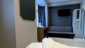 A modern hotel room with a neatly made bed, a large window with curtains, a flat-screen TV mounted on the wall, and a sofa in the background. -  Rest Inn Edmonton (London)