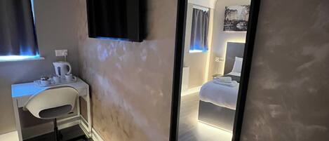 Una habitación de hotel moderna con un espejo grande, un televisor de pantalla plana, un escritorio con silla y una cama con cabecera.