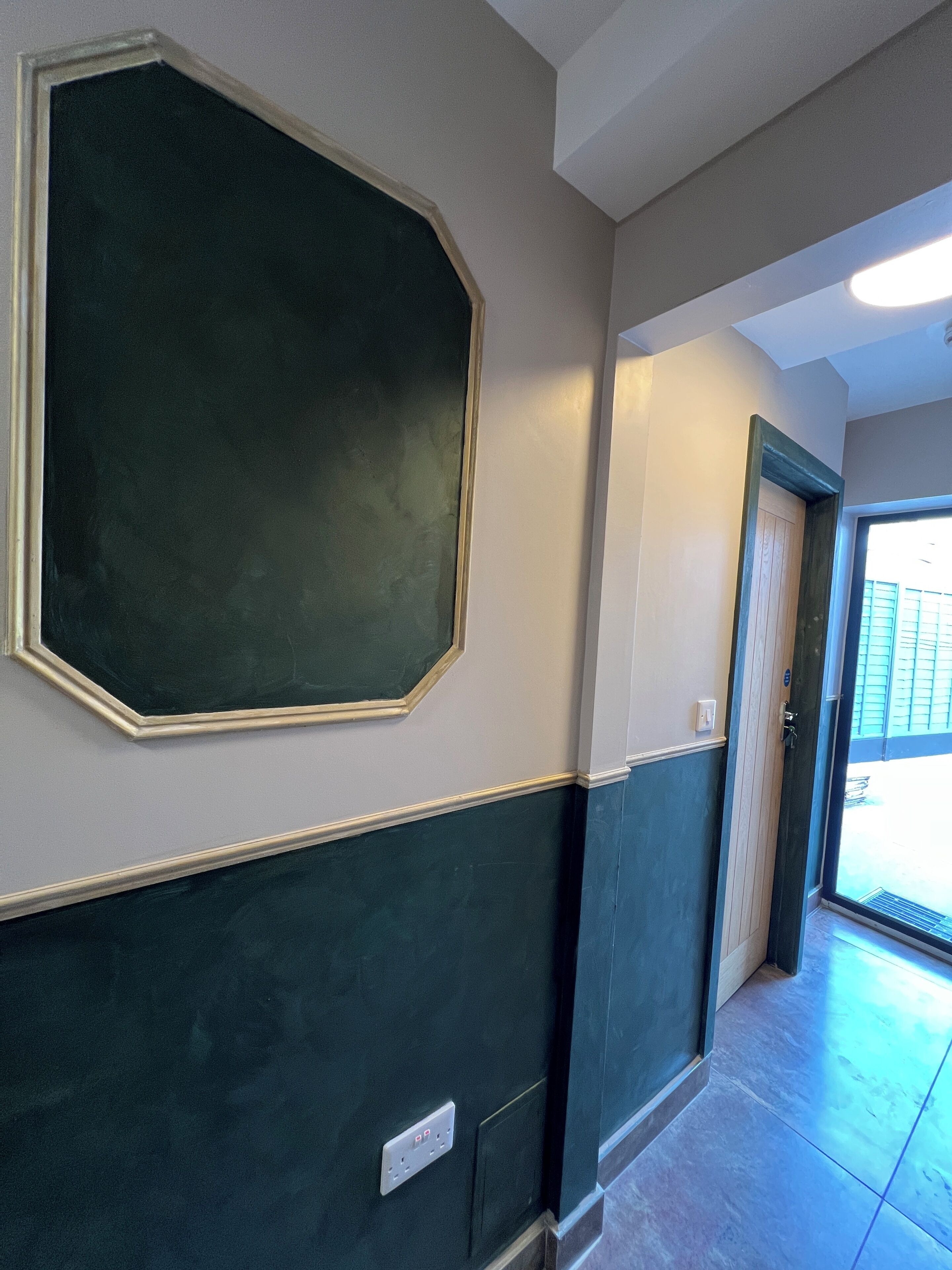 A hallway with a large octagonal mirror on the wall, a door with a keyhole, and a light fixture on the ceiling.