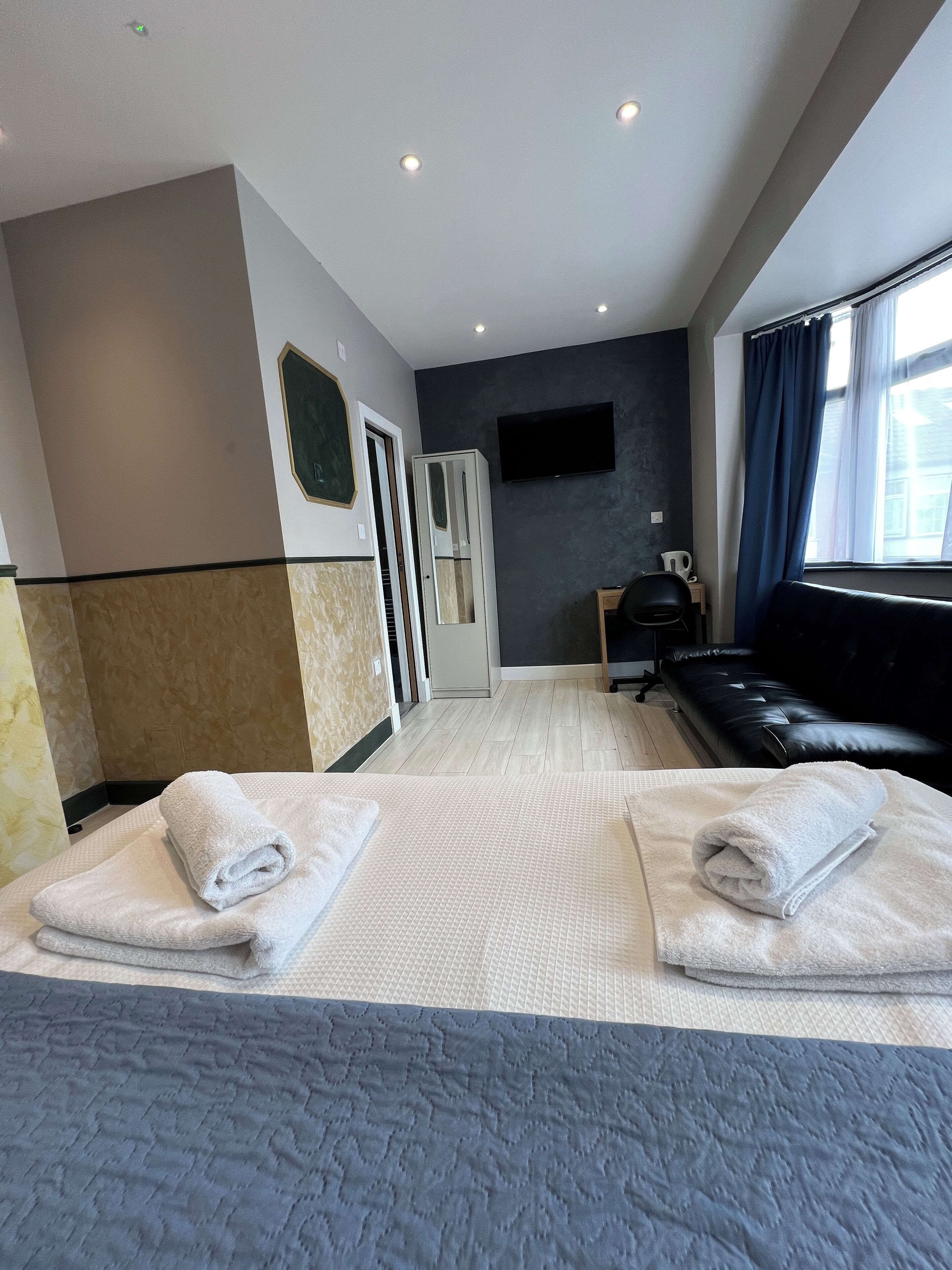 A hotel room with a bed, two towels, a TV, a sofa, and a window with curtains.