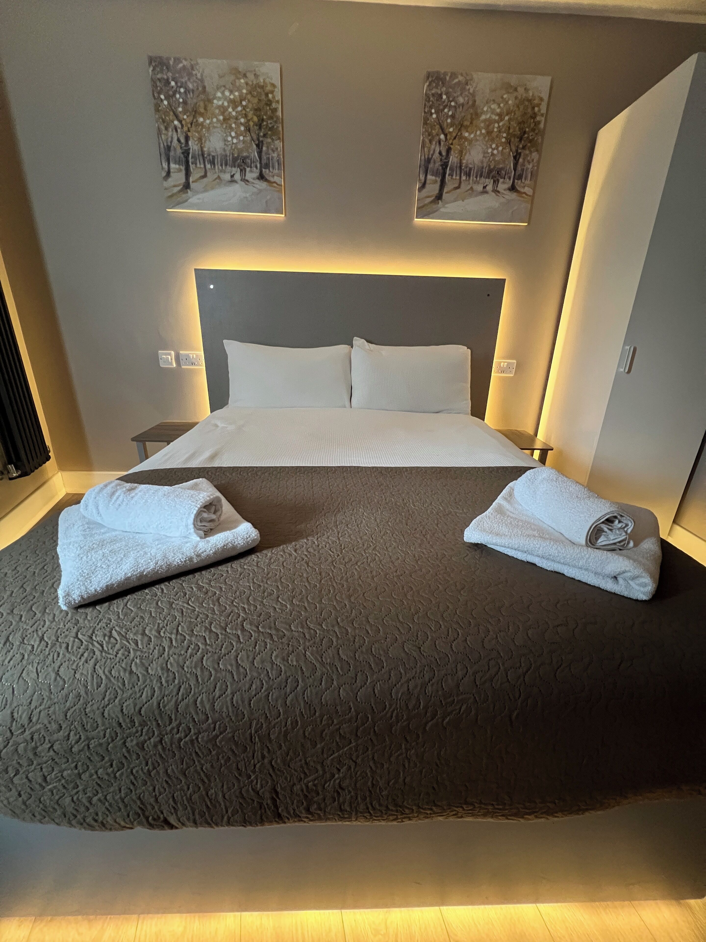 Cama bem arrumada com um edredom escuro texturizado, duas almofadas brancas e duas toalhas dobradas sobre a cama.