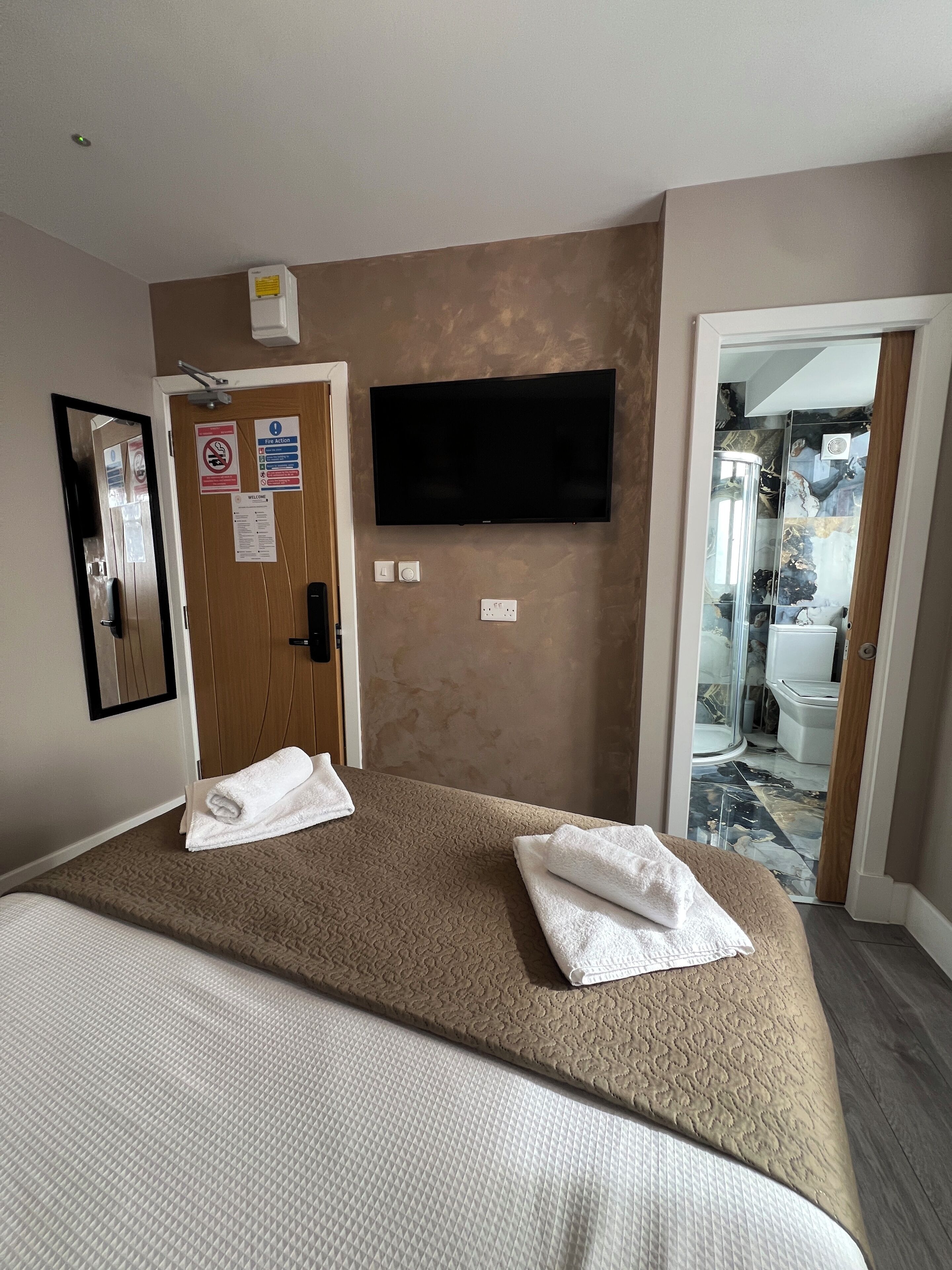 A hotel room with a bed, a flat-screen TV mounted on the wall, and a bathroom visible through an open door.
