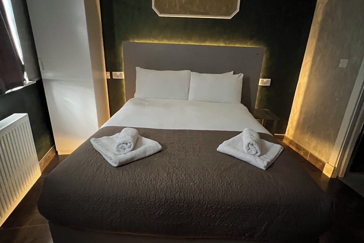 A modern hotel room with a large bed, a headboard with integrated lighting, and a view of the cityscape.