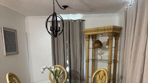 Un comedor con una mesa de vidrio rodeada de sillas ornamentadas, una lámpara de pie decorativa y una mesa auxiliar alta y ornamentada.