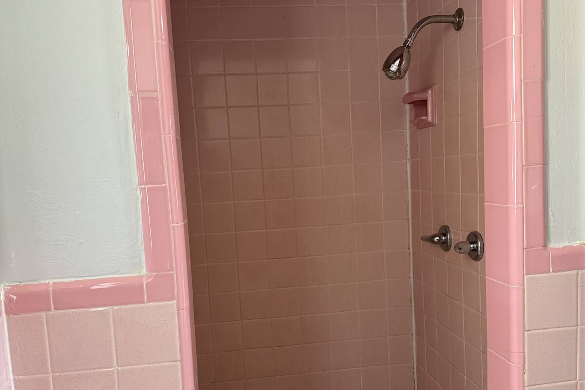 A bathroom with pink and white tiles, a sink with a faucet, and a shower area with a handheld showerhead.