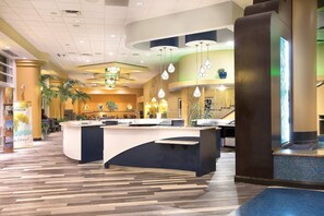 Welcome to our hotel lobby, featuring a contemporary design with a central reception desk and lush greenery.