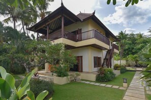A two-story house with a balcony, surrounded by lush greenery and a well-maintained lawn. - Villa Singkenken (Bali)