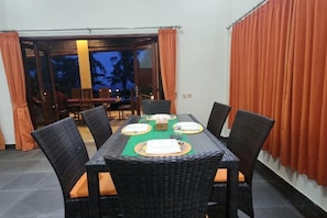 A dining area with a table set for four, surrounded by wicker chairs with cushions. - Villa Singkenken (Bali)