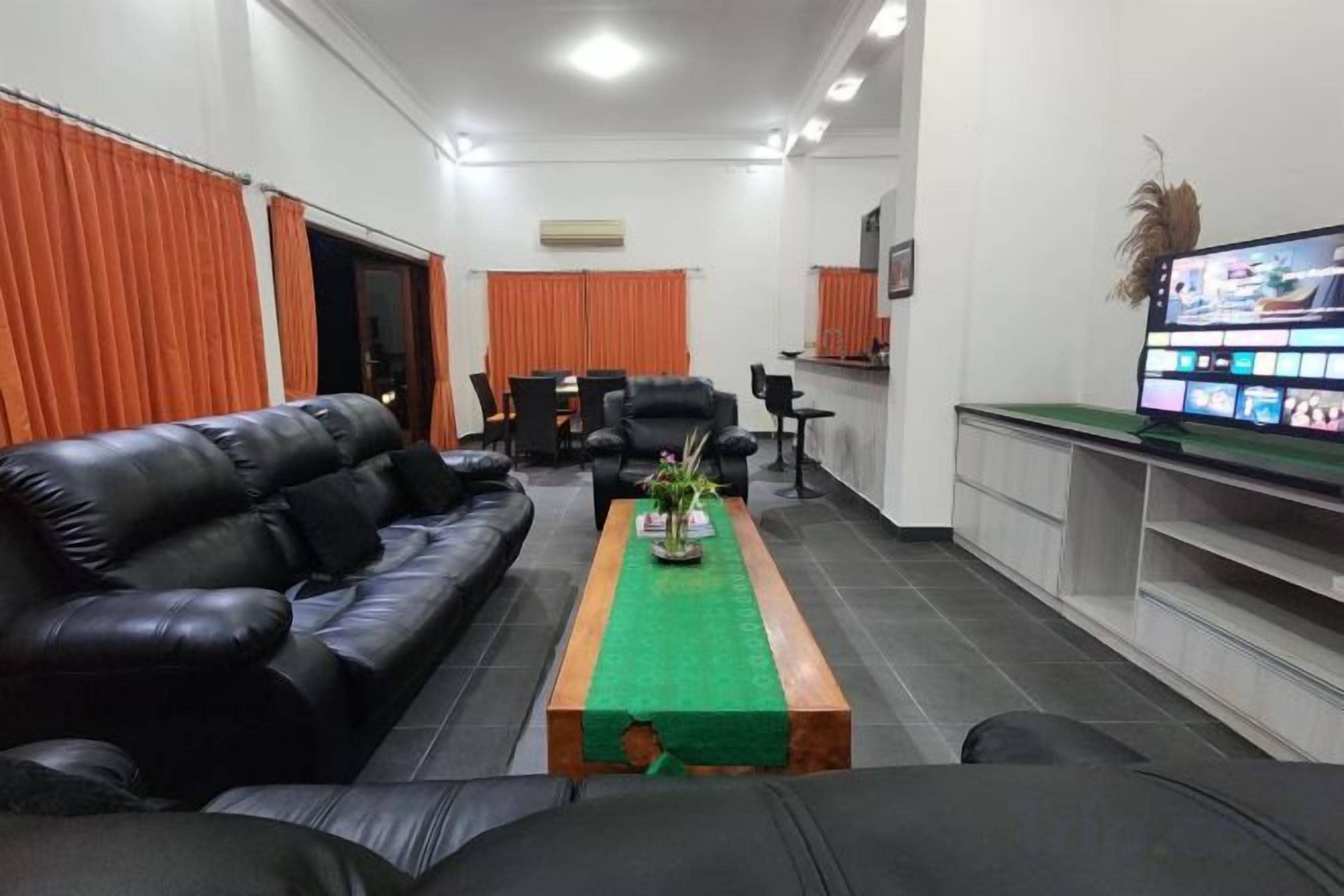 Une chambre d’hôtel avec un canapé en cuir noir, une table basse en bois, un téléviseur à écran plat et un bureau avec un ordinateur.