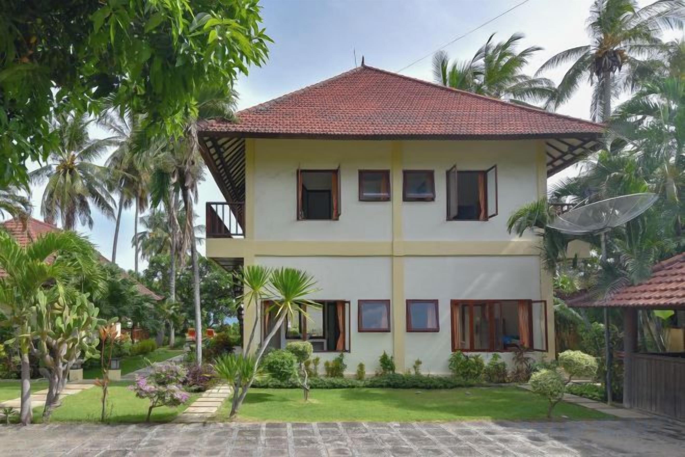 A two-story building with a red-tiled roof, surrounded by greenery and palm trees.