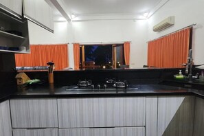 A kitchen with a gas stove, a sink, and a window with curtains. - Villa Singkenken (Bali)