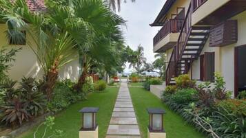 A pathway leading to a building with a staircase, surrounded by lush greenery and palm trees.