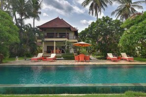 A two-story house with a swimming pool in front, surrounded by palm trees and greenery. - Villa Singkenken (Bali)