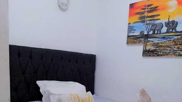 Un lit bien fait, avec une literie à rayures et une tête de lit noire, un oreiller blanc orné d’une broderie « Omil » et une serviette posée sur le lit.