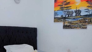 Un lit bien fait, avec une literie à rayures, un oreiller orné d’un motif jaune et deux tableaux représentant des scènes de la vie sauvage, accrochés au mur.