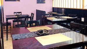 Un restaurant avec plusieurs tables et chaises, un mur rose et des œuvres d’art accrochées au mur.