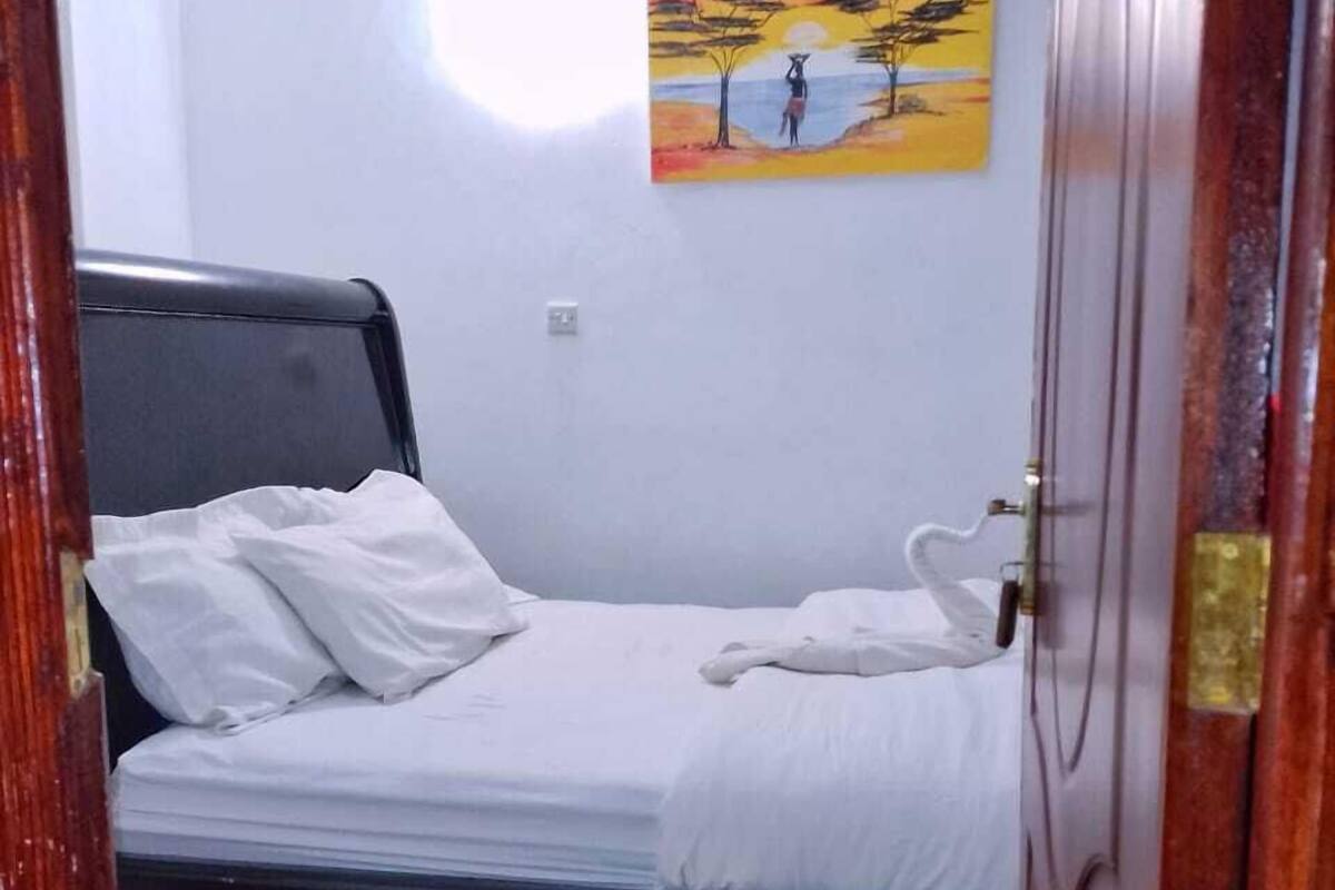Un dormitorio con una cama, ropa de cama blanca, un cuadro en la pared y una puerta de madera.