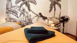 Habitación de hotel con cama, ventilador y un mural de un gato en una rama de árbol.