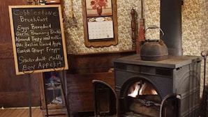 A cozy room with a wood-burning stove, a chalkboard menu listing breakfast items, and a vintage-style wall clock. - Relax in our Parlor Room at The Cobblestone Bed & Breakfast (Birchwood)