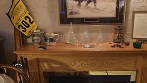 Une cheminée en bois ornée d’un tableau encadré, d’une enseigne jaune et de divers petits objets.