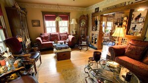 A cozy living room with a red sofa, a wooden cabinet, and a coffee table with various items. - Relax in our Fish Haven Room in the Lower Lodge at The Cobblestone Bed & Breakfast (Birchwood)