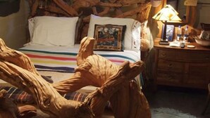 A bed with a wooden headboard, a bedside table with a lamp, and a framed picture on the wall. - Relax in our Fish Haven Room in the Lower Lodge at The Cobblestone Bed & Breakfast (Birchwood)