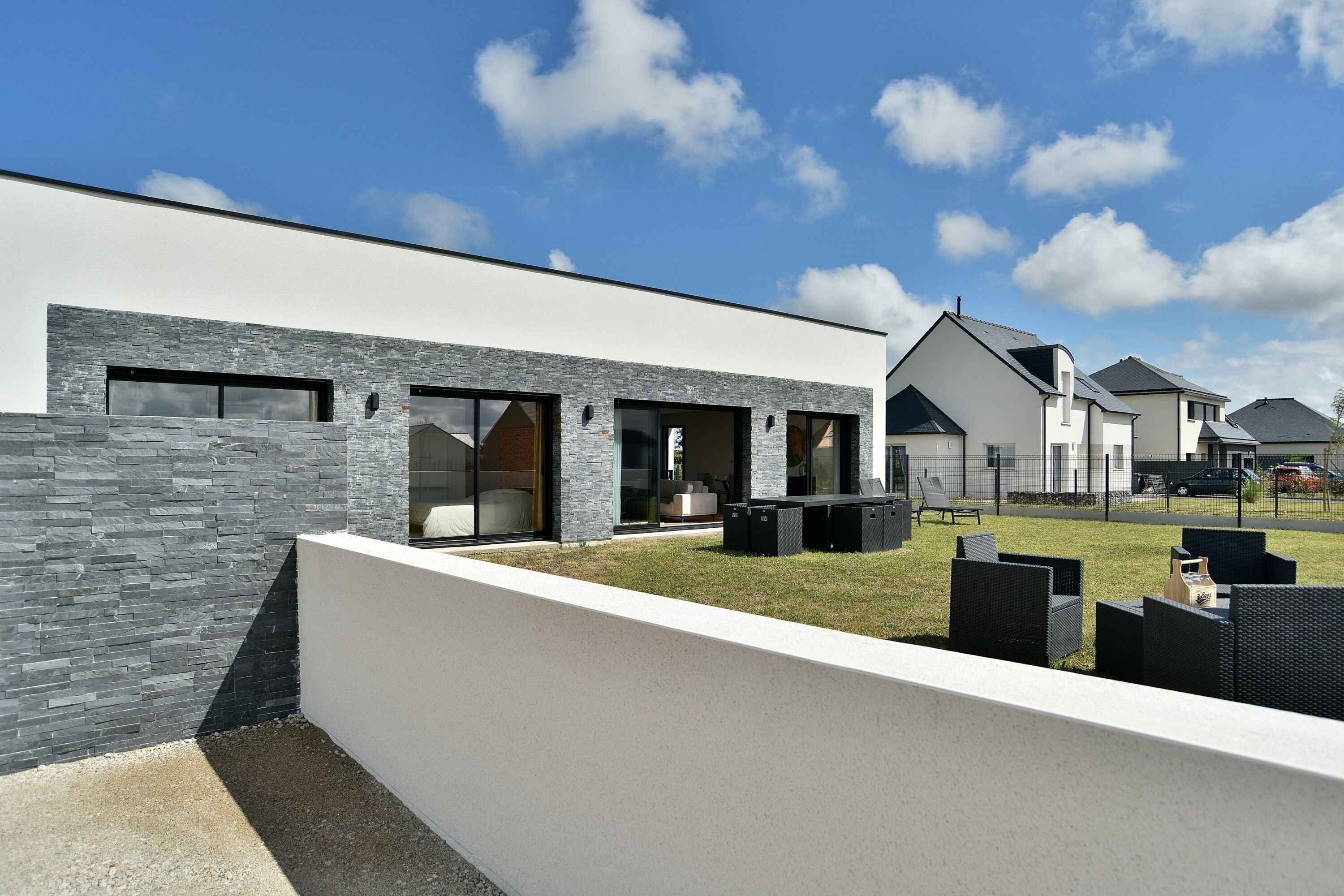 A modern residential building with a stone facade, large windows, and a well-maintained lawn with outdoor furniture.