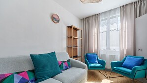 A modern living room with a grey sofa, teal armchairs, a wooden bookshelf, and a round coffee table. - La Halte Sainte-Catherine - Maison à 15min de la plage (Honfleur)