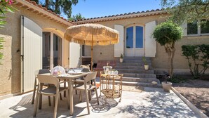 An outdoor patio with a table and chairs, a thatched umbrella, and potted plants. - Chez Nous Baraille - Appt climatisé avec piscine (Puget-sur-Argens)