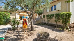A courtyard with a rustic house, a wooden barrel, and a decorative figure. - Chez Nous Baraille - Appt climatisé avec piscine (Puget-sur-Argens)