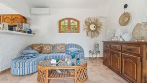 A living room with a striped sofa, a round coffee table, a wooden cabinet, and a wall-mounted mirror. - Chez Nous Baraille - Appt climatisé avec piscine (Puget-sur-Argens)