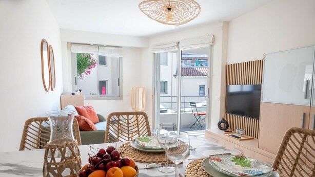 A dining area with a table set for two, featuring a wicker vase, a fruit basket, and a glass of wine. - Le Cocon de la Pinède - Antibes, proche plage (Antibes)