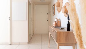 A hallway with a wooden console table, a white door, and a wall with hanging decorative items. - Le Cocon de la Pinède - Antibes, proche plage (Antibes)