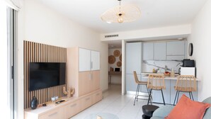 A modern living room with a flat-screen TV, a sofa, a glass coffee table, and a dining area with wicker chairs. - Le Cocon de la Pinède - Antibes, proche plage (Antibes)