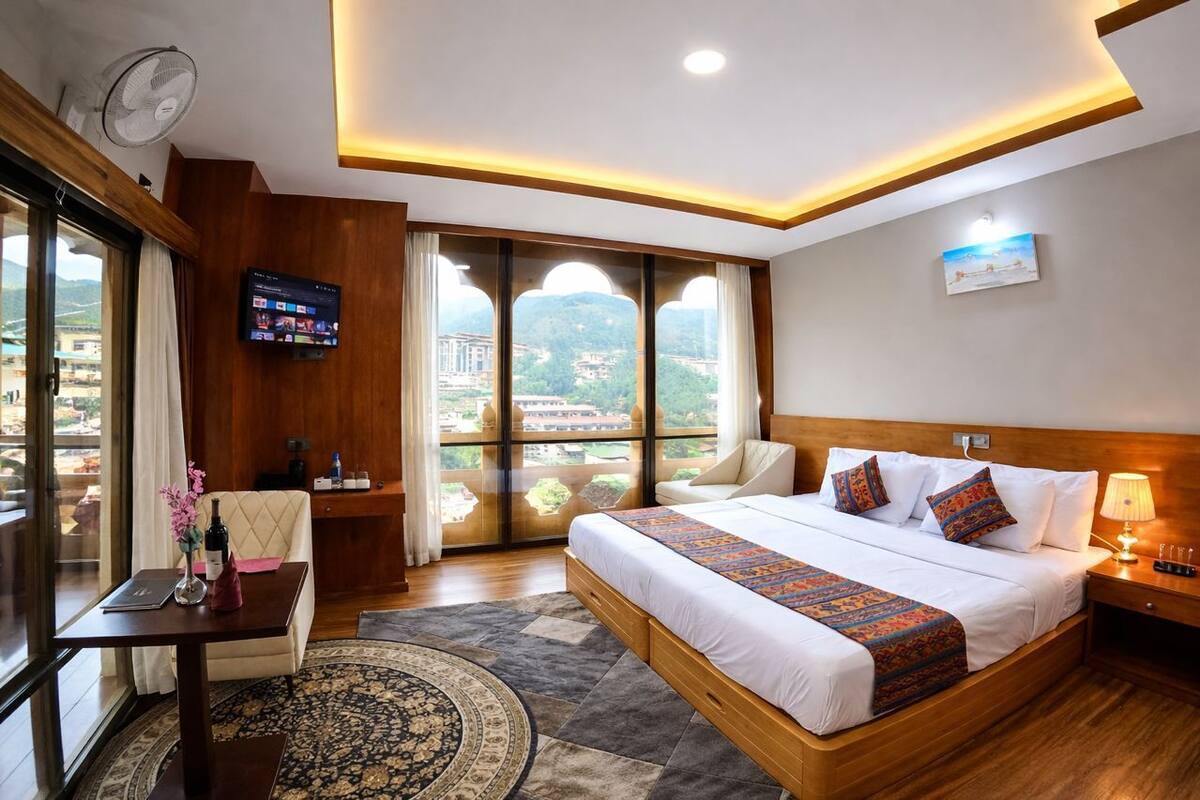 A hotel room with a large bed, a TV, a desk, a chair, and a view of the city.
