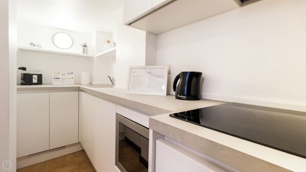 A modern kitchen with white cabinetry, a black induction cooktop, a coffee maker, and a framed menu on the counter. - Italianway Comfort - San Maurilio 20 B (Milan)